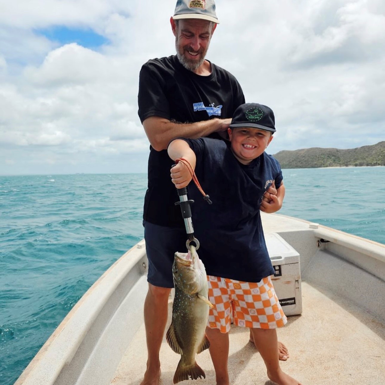 Bella’s partner and son standing on a boat holding a caught fish.