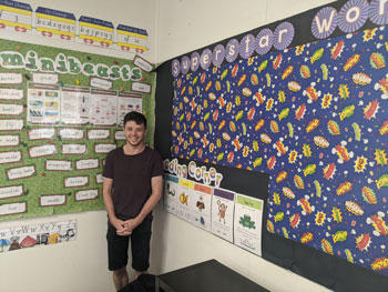 man standing in corner of room in front of walls decorated with learning material